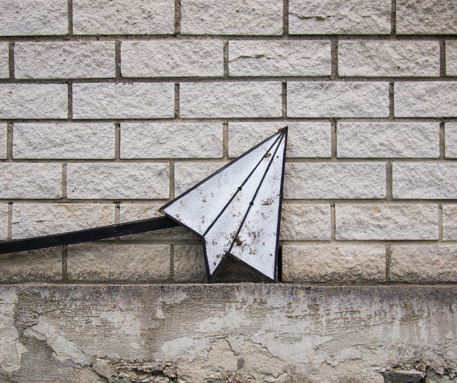 tattered-paper-airplane-sign-fallen-in-front-of-white-brick