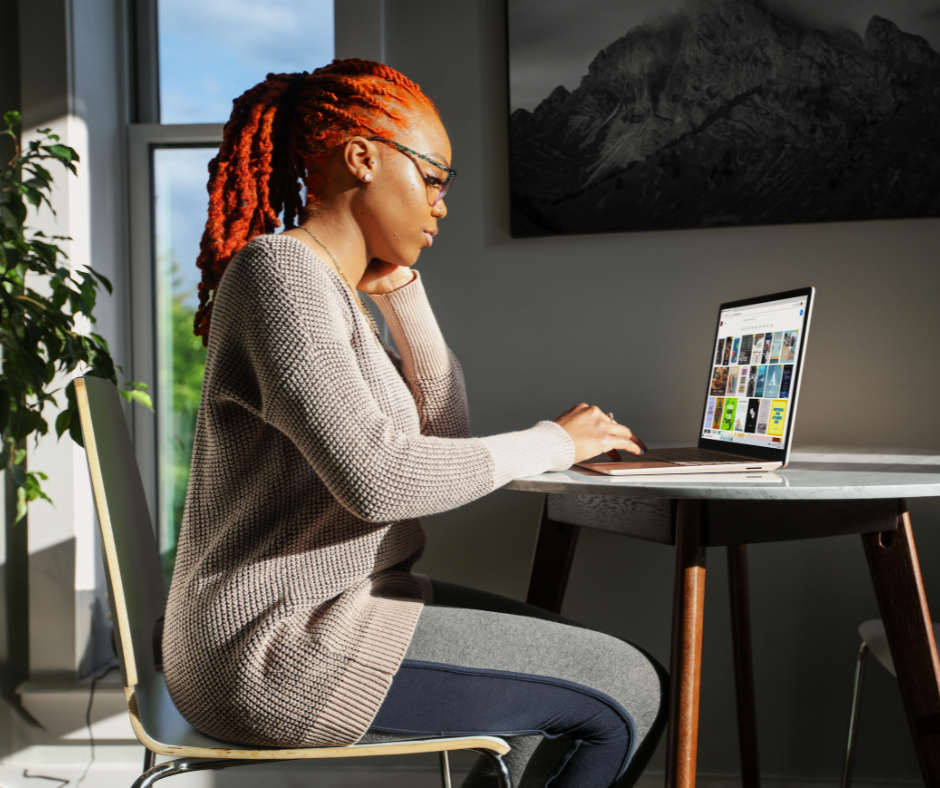 Red haired woman in sweater working from home on a microsoft surface in natural lighting